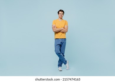 Full body smiling happy fun caucasian young man 20s wear yellow t-shirt hold hnads crossed folded look camera isolated on plain pastel light blue background studio portrait. People lifestyle concept