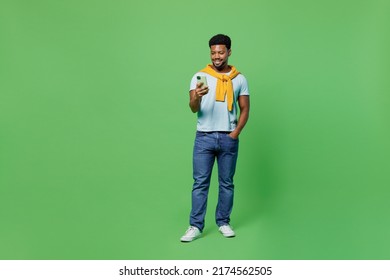 Full Body Smiling Happy Fun Young Man Of African American Ethnicity 20s In Blue T-shirt Hold In Hand Use Mobile Cell Phone Isolated On Plain Green Background Studio Portrait. People Lifestyle Concept