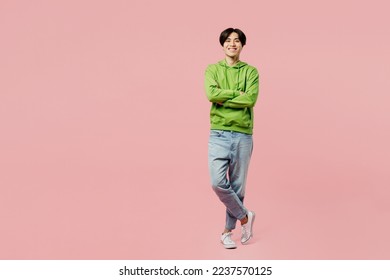 Full body smiling happy fun young man of Asian ethnicity wear green hoody look camera hold hands crossed folded isolated on plain pastel light pink background studio portrait. People lifestyle concept