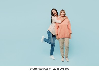 Full body smiling happy fun cheerful cool elder parent mom with young adult daughter two women together wear casual clothes look camera hugging isolated on plain blue background. Family day concept