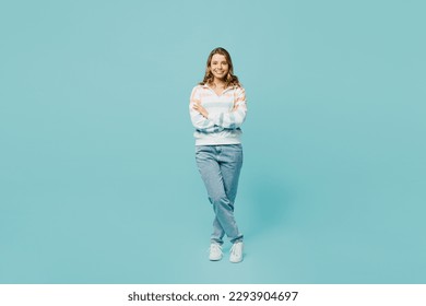 Full body smiling happy fun cheerful young woman wearing striped hoody look camera holding hands crossed folded isolated on plain pastel light blue cyan background studio portrait. Lifestyle concept