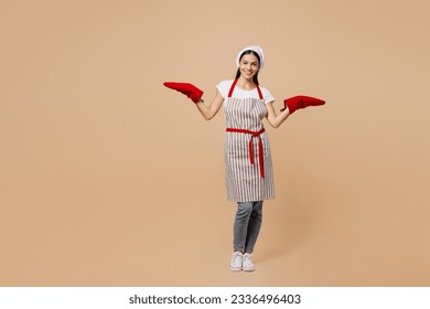 Full body smiling happy fun young housewife housekeeper chef baker latin woman wear apron toque hat spread hands in gloves potholders isolated on plain pastel light beige background. Cook food concept - Powered by Shutterstock