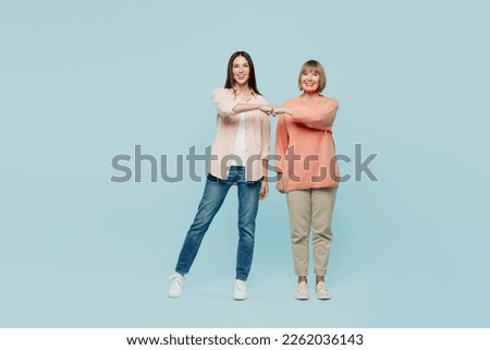 Full body smiling happy fun cheerful confident elder parent mom with young adult daughter two women together wear casual clothes give fist bump isolated on plain blue background. Family day concept