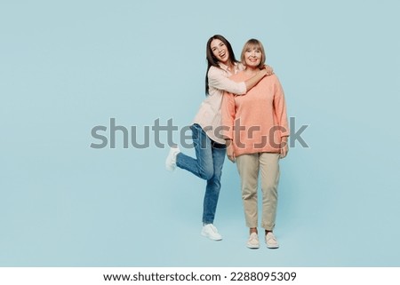 Full body smiling happy fun cheerful cool elder parent mom with young adult daughter two women together wear casual clothes look camera hugging isolated on plain blue background. Family day concept