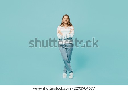 Full body smiling happy fun cheerful young woman wearing striped hoody look camera holding hands crossed folded isolated on plain pastel light blue cyan background studio portrait. Lifestyle concept