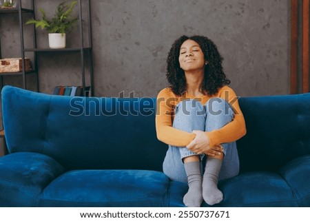 Full body smiling happy fun little kid teen girl wear casual clothes close eyes sits on blue sofa couch stay at home hotel flat rest relax spend free spare time in living room indoor. Lounge concept