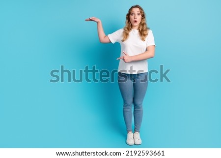 Full body smiling happy woman point index finger aside length isolated blue background studio portrait.
