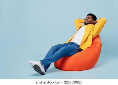 Full body smiling happy young man of African American ethnicity wear yellow shirt sit in bag chair look camera hold hands behind neck isolated on plain pastel light blue background studio portrait. - Powered by Shutterstock