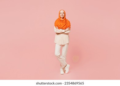 Full body smiling happy young arabian asian muslim woman wears orange abaya hijab hold hands crossed folded look camera isolated on plain pink background. Uae middle eastern islam religious concept - Powered by Shutterstock