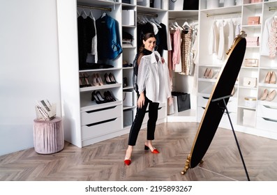 Full Body Of Smiling Woman In Stylish Outfit Standing In Living Room Near Mirror Against White Closet And Dressing Up At Home