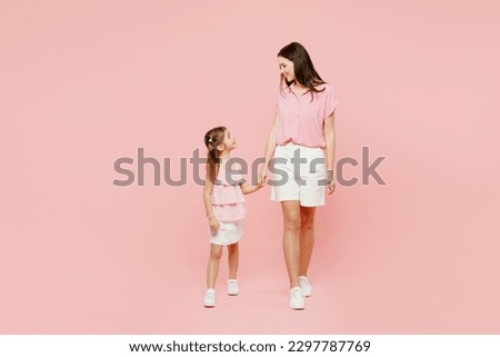 Full body smiling woman wear casual clothes with child kid girl 6-7 years old. Mother daughter look to each other hold hands walk isolated on plain pastel pink background. Family parent day concept
