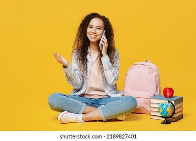 Full Body Smiling Young Black Teen Girl Student Wear Casual Clothes Backpack Bag Sit Talk Speak On Mobile Cell Phone Isolated On Plain Yellow Color Background High School University College Concept