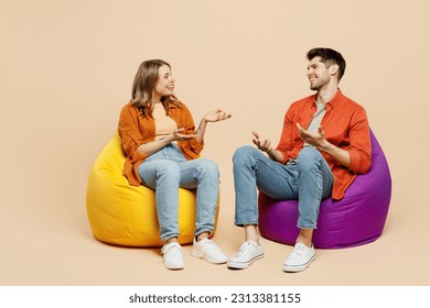 Full body smiling young couple two friends family man woman wear casual clothes together sit in bag chair talk speak spread hands isolated on pastel plain light beige color background studio portrait - Shutterstock ID 2313381155