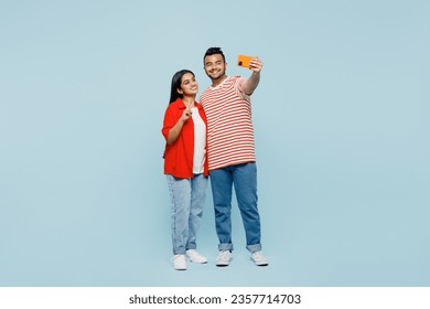 Full body smiling young couple two friends family Indian man woman wear red casual clothes t-shirts together do selfie shot mobile cell phone post photo show v-sign isolated on plain blue background