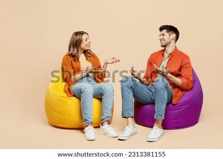 Full body smiling young couple two friends family man woman wear casual clothes together sit in bag chair talk speak spread hands isolated on pastel plain light beige color background studio portrait