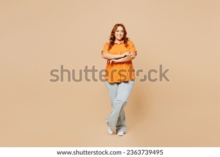 Full body smiling young ginger chubby overweight woman wears orange shirt casual clothes hold hands crossed folded isolated on plain pastel light beige background studio portrait. Lifestyle concept