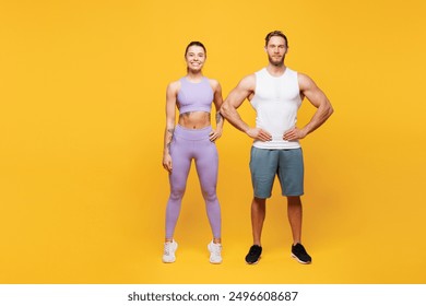 Full body smiling young strong fitness trainer sporty two man woman wearing blue clothes spend time in home gym stand akimbo look camera isolated on plain yellow background. Workout sport fit concept - Powered by Shutterstock