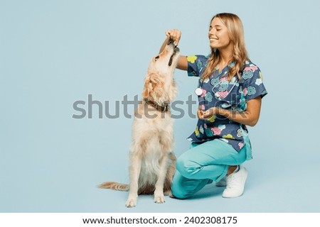 Full body smiling young veterinarian woman wear uniform stethoscope heal exam feed give pill to retriever dog isolated on plain pastel light blue background studio portrait. Pet health care concept
