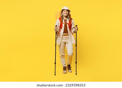 Full body smiling young woman carry bag with stuff mat hold trekking poles isolated on plain yellow background. Tourist leads active lifestyle walk on spare time. Hiking trek rest travel trip concept - Shutterstock ID 2329398353
