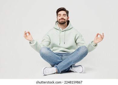 Full body spiritual tranquil young man wear mint hoody hold spreading hands in yoga om aum gesture relax meditate try to calm down isolated on plain solid white background. People lifestyle concept - Powered by Shutterstock