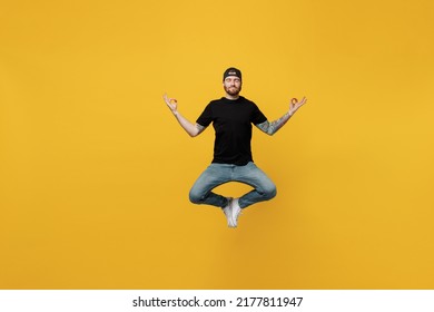 Full Body Spiritual Young Bearded Tattooed Man 20s He Wear Casual Black T-shirt Cap Hold Spreading Hands In Yoga Om Aum Gesture Relax Meditate Try To Calm Down Isolated On Plain Yellow Wall Background