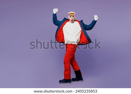 Full body strong winner cool skier man wear warm blue windbreaker jacket ski goggles mask hat show muscles on hand spend extreme weekend winter season in mountains isolated on plain purple background