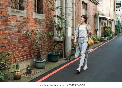 Full body of stylish short haircut positive young aged female in jeans and sneakers strolling along old Taiwan street near modern building at Taipei