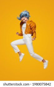 Full Body Of Stylish Teen Female Model With Dyed Hair Wearing Trendy Leather Jacket And White Pants Jumping Against Yellow Background