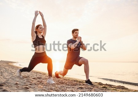 Full body sunlit couple young two friend sporty sportswoman sportsman woman man in sport clothes warm up training do lunges do exercise on sand sea ocean beach outdoor on seaside in summer day morning