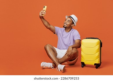Full body traveler black man wear t-shirt hat do selfie shot on mobile cell phone isolated on plain orange background. Tourist travel abroad in spare time rest getaway. Air flight trip journey concept