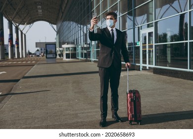 Full Body Traveler Businessman Young Man In Black Suit Sterile Facial Mask Stand Outside At International Airport Terminal With Suitcase Do Selfie Shot On Mobile Cell Phone Air Flight Business Concept