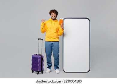 Full body traveler man wear casual clothes hold passport ticket near blank screen mobile phone valise isolated on plain grey background Tourist travel abroad in free time rest Air flight trip concept