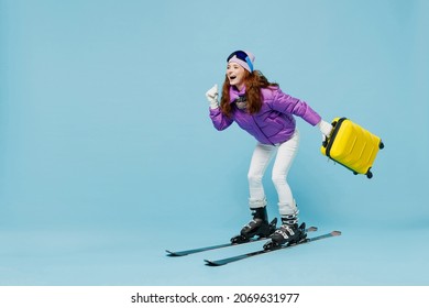Full body traveler tourist woman in winter ski windbreaker jacket goggles hold valise suitacase isolated on plain blue background studio Passenger travel abroad weekends getaway Air flight concept.