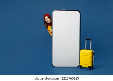 Full body traveler woman wear sweater red hat yellow raincoat big huge blank screen area mobile cell phone with bag travel abroad in free time isolated on plain dark blue background Getaway concept - Shutterstock ID 2226760223