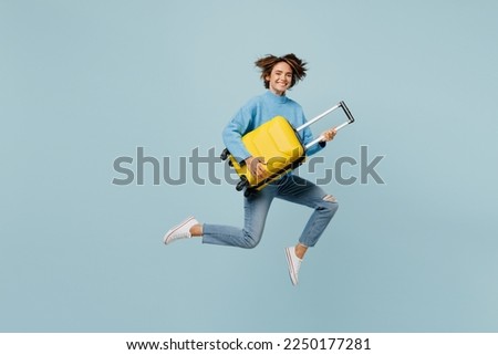 Full body traveler woman wear sweater hold suitcase run isolated on plain pastel light blue cyan color background studio. Tourist travel abroad in free spare time rest getaway Air flight trip concept
