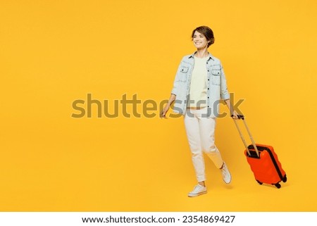 Full body traveler woman wears casual clothes denim shirt hold suitcase walk isolated on plain yellow background. Tourist travel abroad in free spare time rest getaway. Air flight trip journey concept