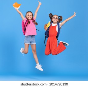 Full body of two happy energetic primary schoolgirls  wearing casual clothes holding backpackand copybook in hands and jumping high against blue background - Powered by Shutterstock