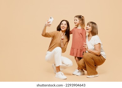 Full body women wear casual clothes with child kid girl 6-7 years old. Granny mother daughter do selfie shot mobile cell phone show v-sign isolated on plain beige background. Family parent day concept