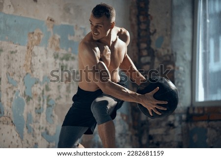 Full body workout. Young muscular man with strong, relief body shape training shirtless with fitness ball indoors. Sweat body. Concept of sportive lifestyle, body care, fitness, hobby, health