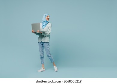 Full Body Young Arabian Asian Muslim Woman In Abaya Hijab Hold Use Work On Laptop Pc Computer Look Aside Isolated On Plain Blue Background Studio. People Uae Middle Eastern Islam Religious Concept.