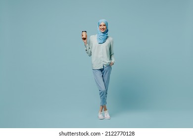 Full body young arabian asian muslim woman in abaya hijab hold takeaway delivery craft paper brown cup coffee to go isolated on plain blue background. People uae middle eastern islam religious concept - Powered by Shutterstock