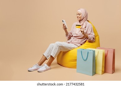 Full body young arabian asian muslim woman she wear abaya hijab sit in bag chair hold mobile phone credit card shopping isolated on plain light beige background. People uae islam religious concept. - Shutterstock ID 2177432581