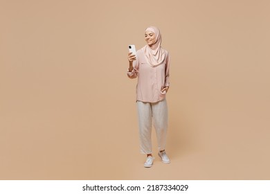 Full body young arabian asian muslim woman she in abaya hijab pink clothes hold use mobile cell phone isolated on plain pastel light beige background People uae middle eastern islam religious concept - Shutterstock ID 2187334029