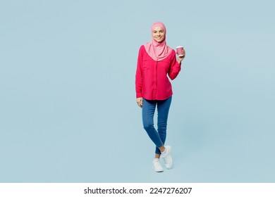 Full body young arabian asian muslim woman wear pink abaya hijab hold takeaway delivery paper cup coffee to go isolated on plain pastel light blue cyan background People uae islam religious concept - Powered by Shutterstock