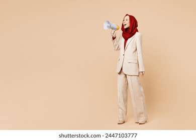 Full body young Arabian Asian Muslim woman wear red abaya hijab suit clothes scream in megaphone announces discounts sale Hurry up isolated on plain beige background. UAE middle eastern Islam concept - Powered by Shutterstock