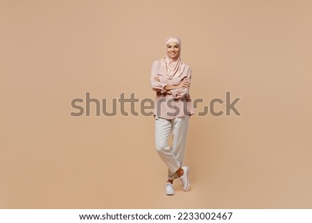 Full body young arabian asian muslim woman she wear abaya hijab pink clothes hold hands crossed folded isolated on plain pastel light beige background People uae middle eastern islam religious concept