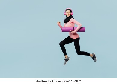 Full body young asian muslim fitness trainer sporty woman wear pink abaya hijab headphones hold yoga mat spend time in home gym isolated on plain blue background studio. Workout sport fit abs concept - Powered by Shutterstock