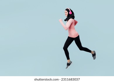 Full body young asian muslim fitness trainer sporty woman wear pink abaya hijab headphones listen music spend time in gym run jump high isolated on plain blue background studio. sport fit abs concept - Powered by Shutterstock