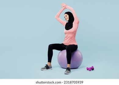 Full body young asian muslim fitness trainer sporty woman wears pink abaya hijab spend time in home gym train do hands stretch lunge exercise isolated on plain blue background Sport fit abs concept - Powered by Shutterstock