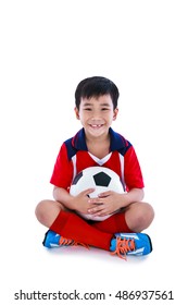 Full body of young asian soccer player in sportswear tooth smile and holding his soccer ball. Cheerful little boy sitting on the floor at studio. Isolated on white background. Positive emotion.